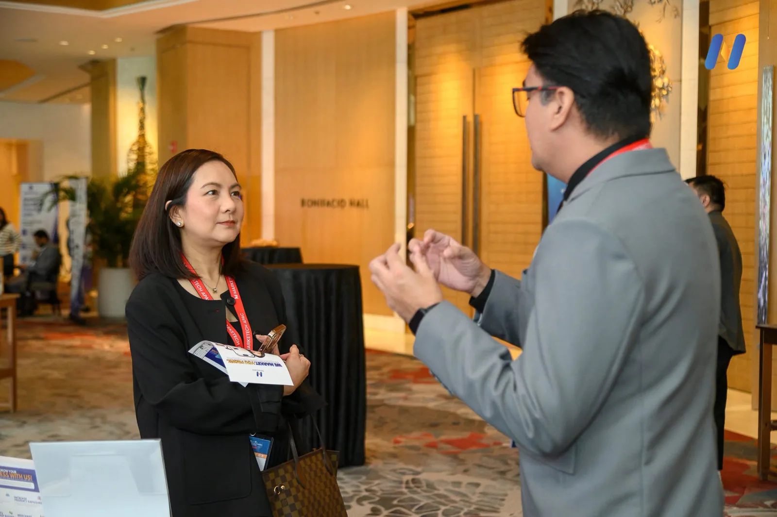 Novaluxia dispatch photo of two attendees talking in the registration area at Shangri-La The Fort during REPH 2026, lanyards on and a phone in hand