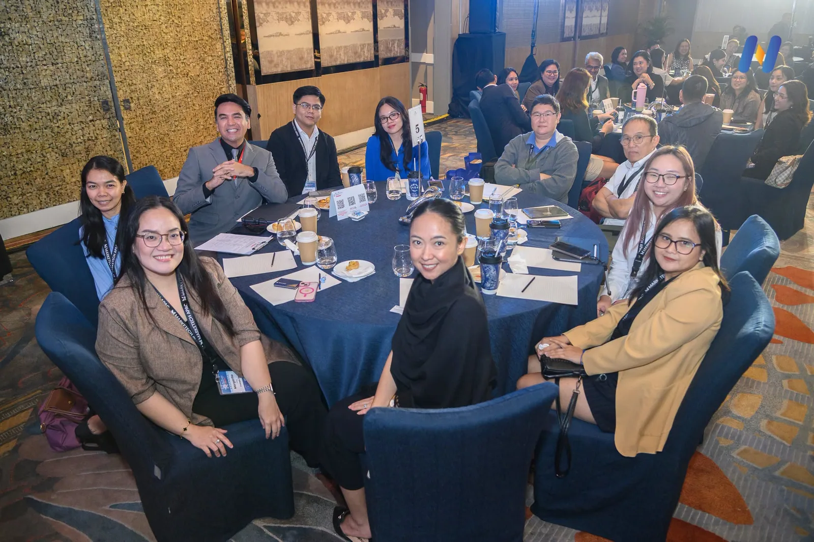 A Novaluxia PH photograph of the roundtable room at the ASEAN FinTech Summit Manila 2026, delegates seated around the round tables with name cards and water glasses set out